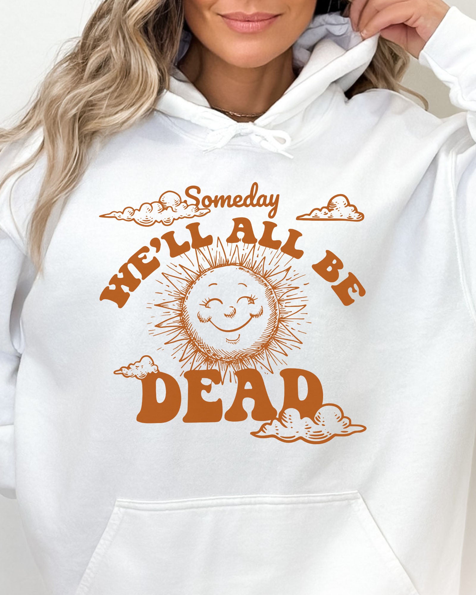 Close-up of a woman wearing a white hoodie featuring a funny retro-style laughing sun graphic and the quote 'Someday We'll All Be Dead'.