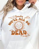Close-up of a woman wearing a white hoodie featuring a funny retro-style laughing sun graphic and the quote 'Someday We'll All Be Dead'.
