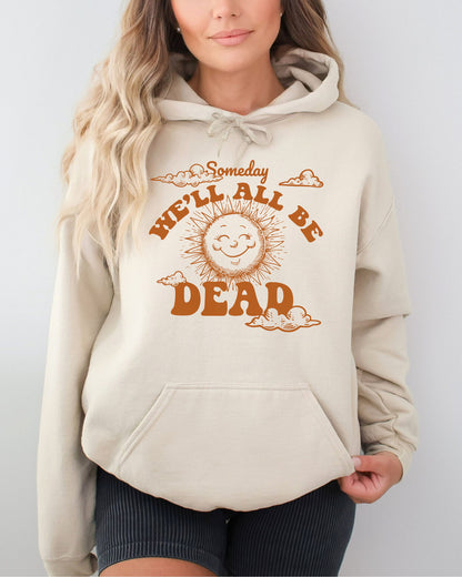 Woman wearing a sand beige hoodie featuring a funny retro-style laughing sun graphic and the quote 'Someday We'll All Be Dead'.