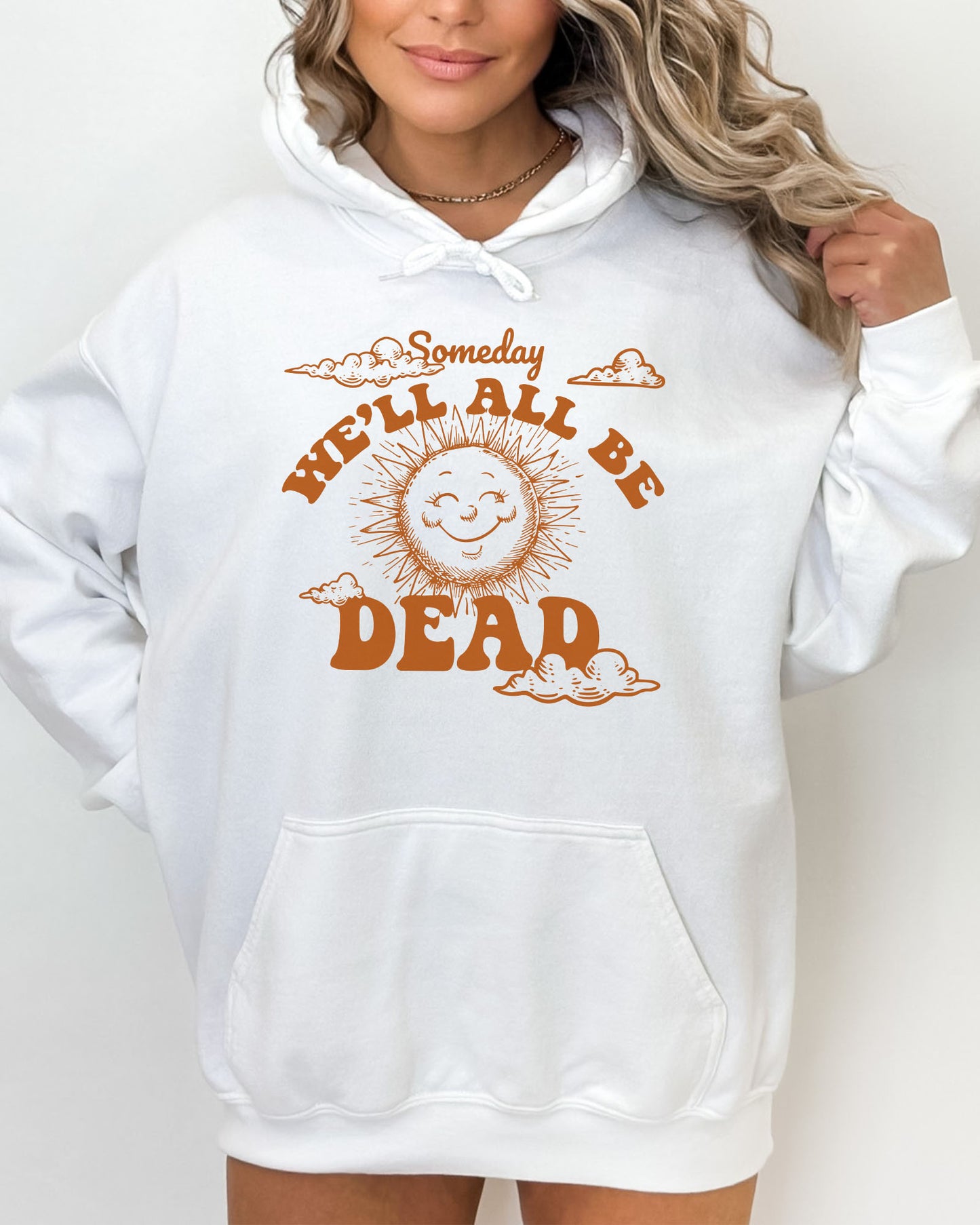 Woman wearing a white hoodie featuring a funny retro-style laughing sun graphic and the quote 'Someday We'll All Be Dead'.