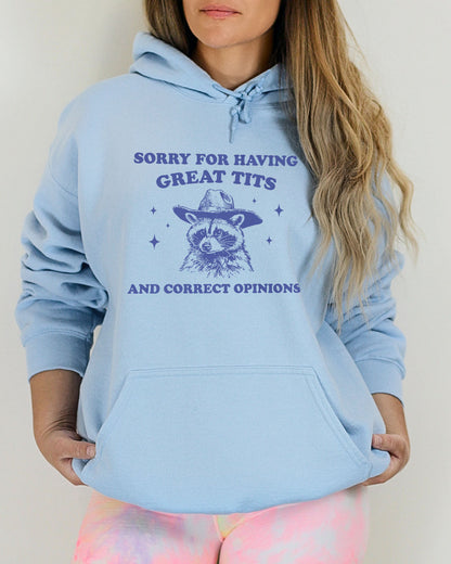 Woman wearing a light blue hoodie with a funny retro cowboy raccoon graphic and the phrase 'Sorry For Having Great Tits And Correct Opinions'.