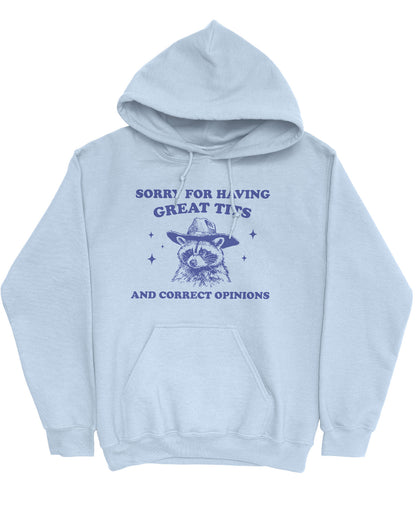 Flat lay of a light blue hoodie with a funny retro cowboy raccoon graphic and the phrase 'Sorry For Having Great Tits And Correct Opinions'.