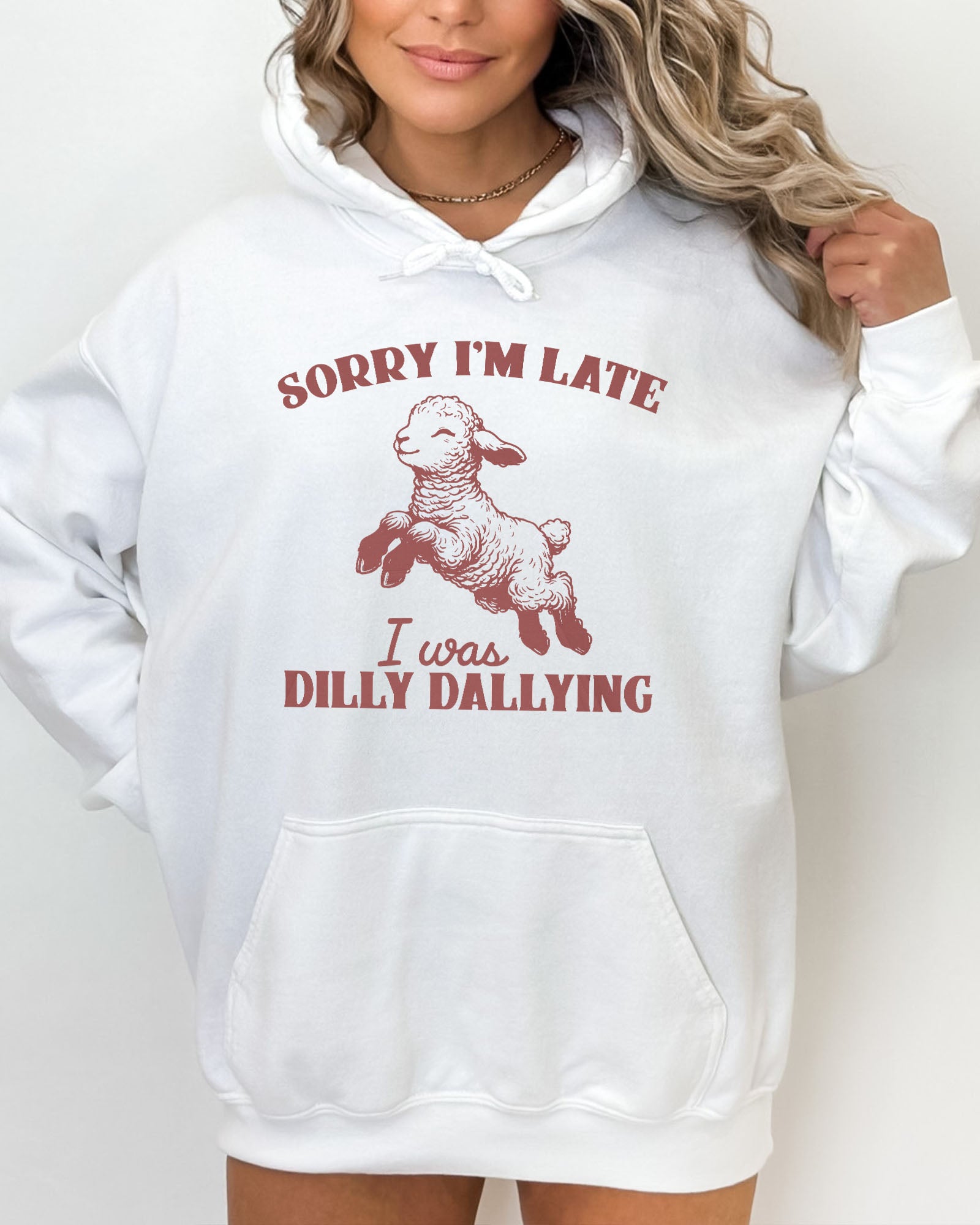 Woman wearing a white hoodie featuring a funny retro-style baby sheep graphic and the quote 'Sorry I'm Late, I Was Dilly Dallying '.