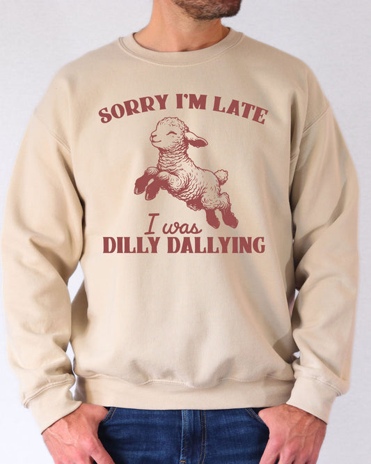 Man wearing a sand beige sweatshirt featuring a funny retro-style sheep graphic and the quote 'Sorry I'm Late, I Was Dilly Dallying'.