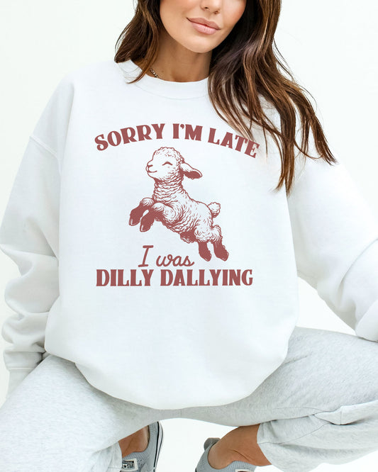 Woman wearing a white sweatshirt featuring a funny retro-style sheep graphic and the quote 'Sorry I'm Late, I Was Dilly Dallying'.