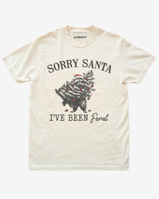Sorry Santa I've Been Feral shirt in ivory with raccoon eating Christmas tree graphic