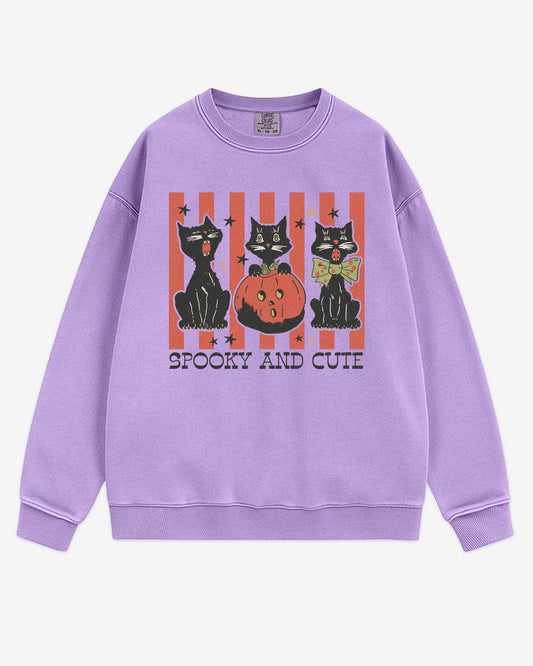 Flat lay orchid-colored 'Spooky And Cute' sweatshirt with retro Halloween graphic of three black cats and a pumpkin.
