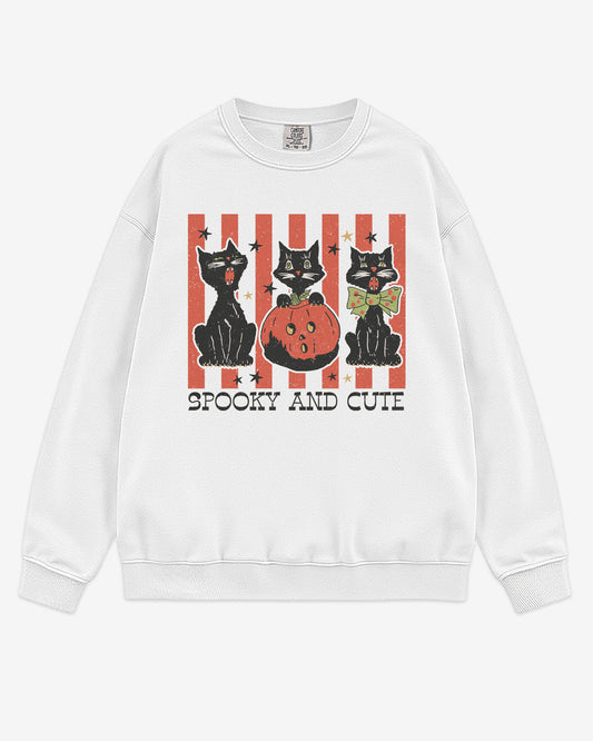 Flat lay white-colored 'Spooky And Cute' sweatshirt with retro Halloween graphic of three black cats and a pumpkin.