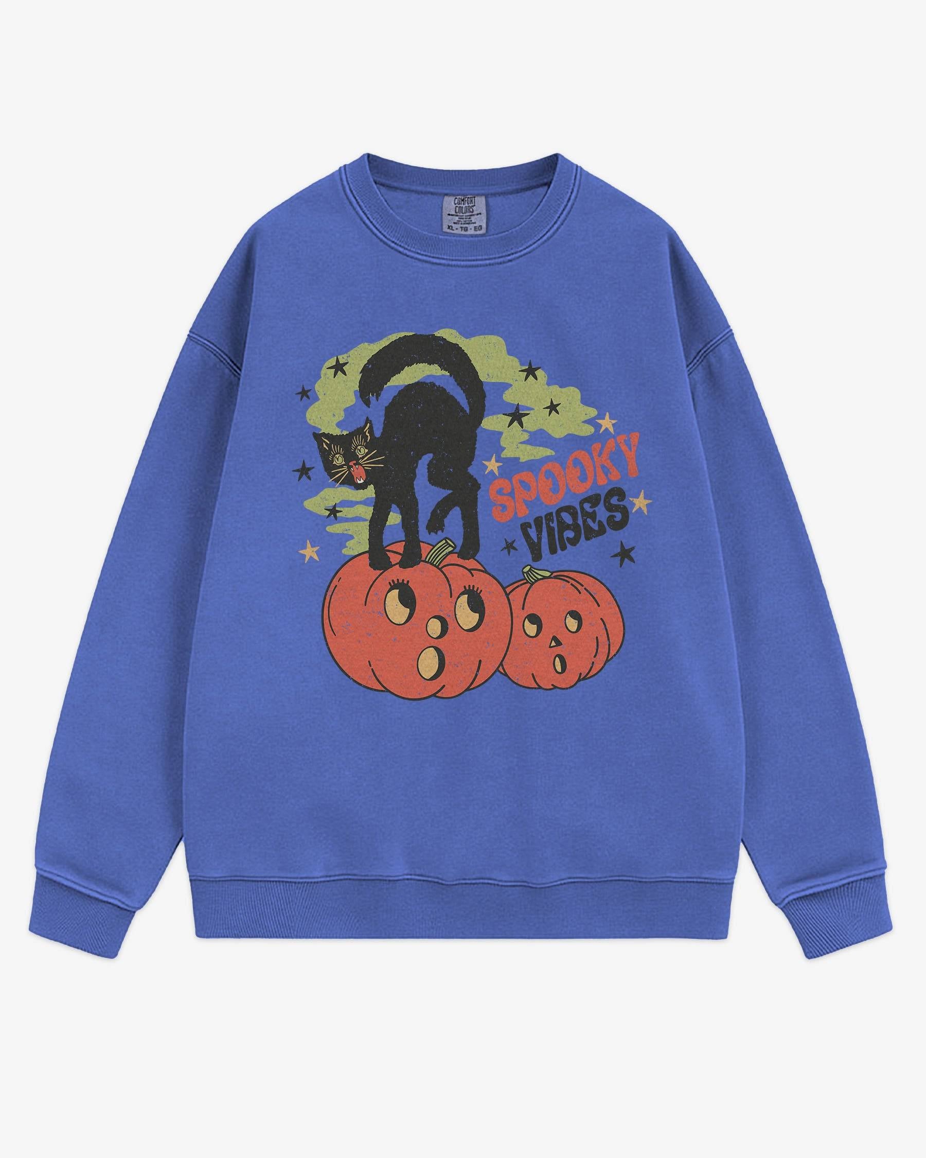 Flat lay flo blue Halloween sweatshirt reading ‘Spooky Vibes’ with retro graphic of black cat standing on pumpkins.
