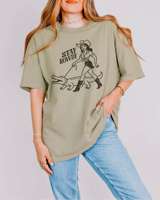 Model wearing khaki color shirt with 'Stay Rowdy' cowgirl walking alligator graphic design