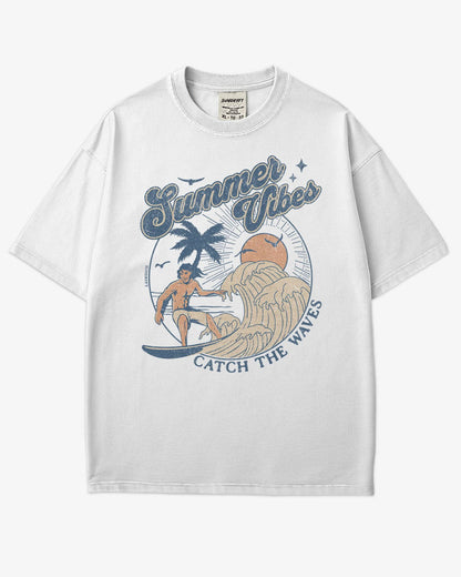 Flat lay white 'Summer Vibes – Catch the Waves' surf shirt with a retro graphic of a surfer riding a wave on the beach.