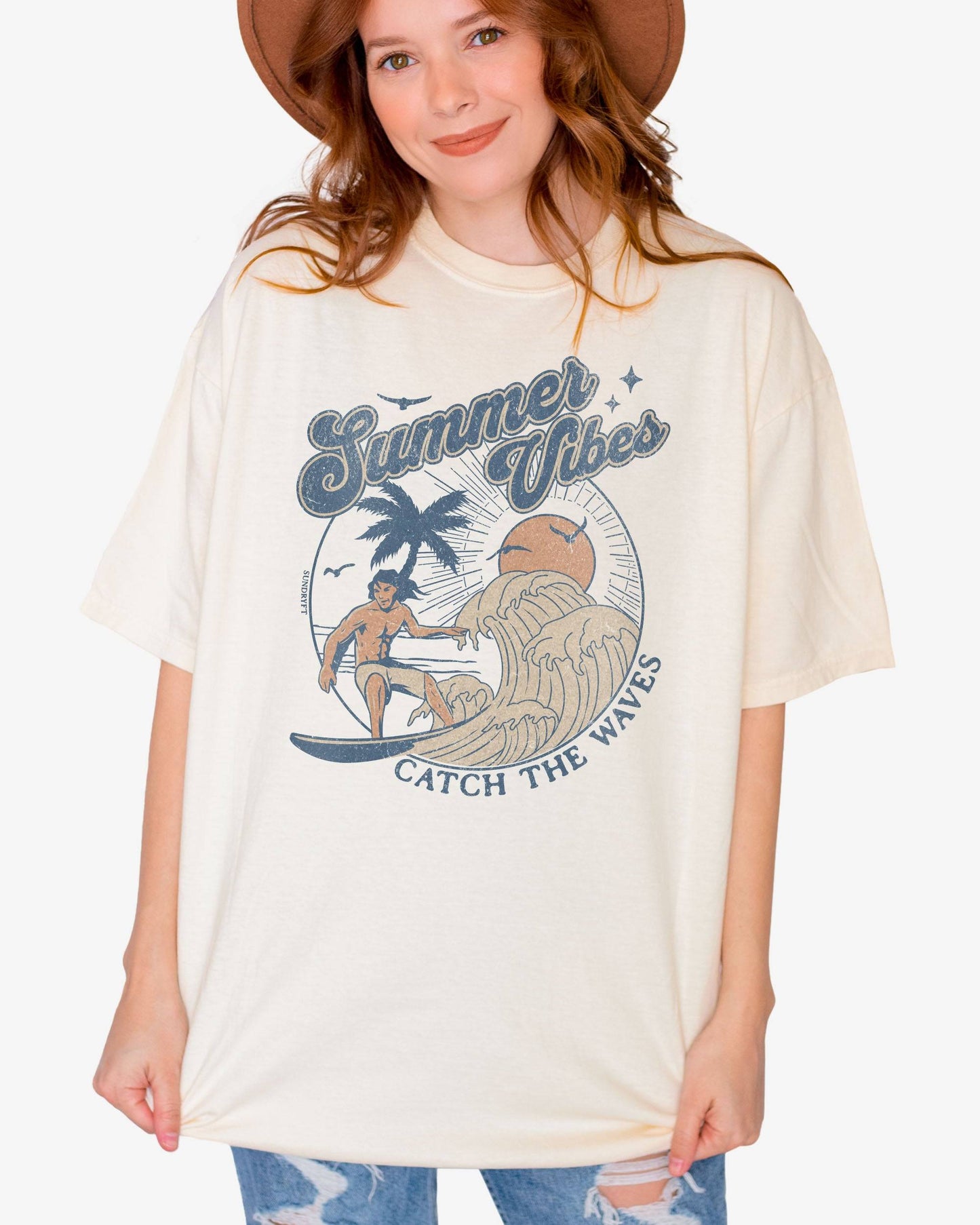 Woman wearing an ivory 'Summer Vibes – Catch the Waves' surf shirt with a retro graphic of a surfer riding a wave on the beach.