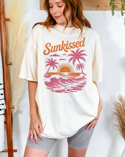 Woman wearing an ivory-colored 'Sunkissed' shirt with a retro graphic of a sunny beach and ocean waves.