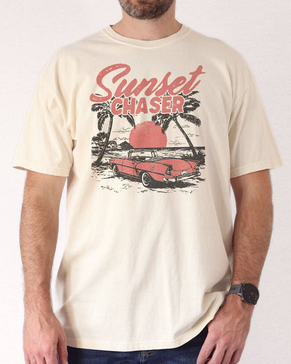 Man wearing ivory shirt with the quote "Sunset Chaser" and a retro car on a beach scenery graphic.