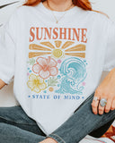Close-up of woman wearing a white "Sunshine State of Mind" shirt with a retro graphic of outlined flowers, sun, and waves.