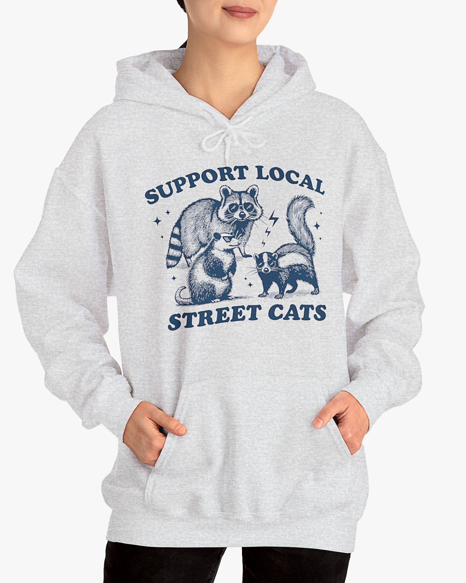 Woman wearing ash gray 'Support Local Street Cats' hoodie with a funny raccoon and opossum retro graphic