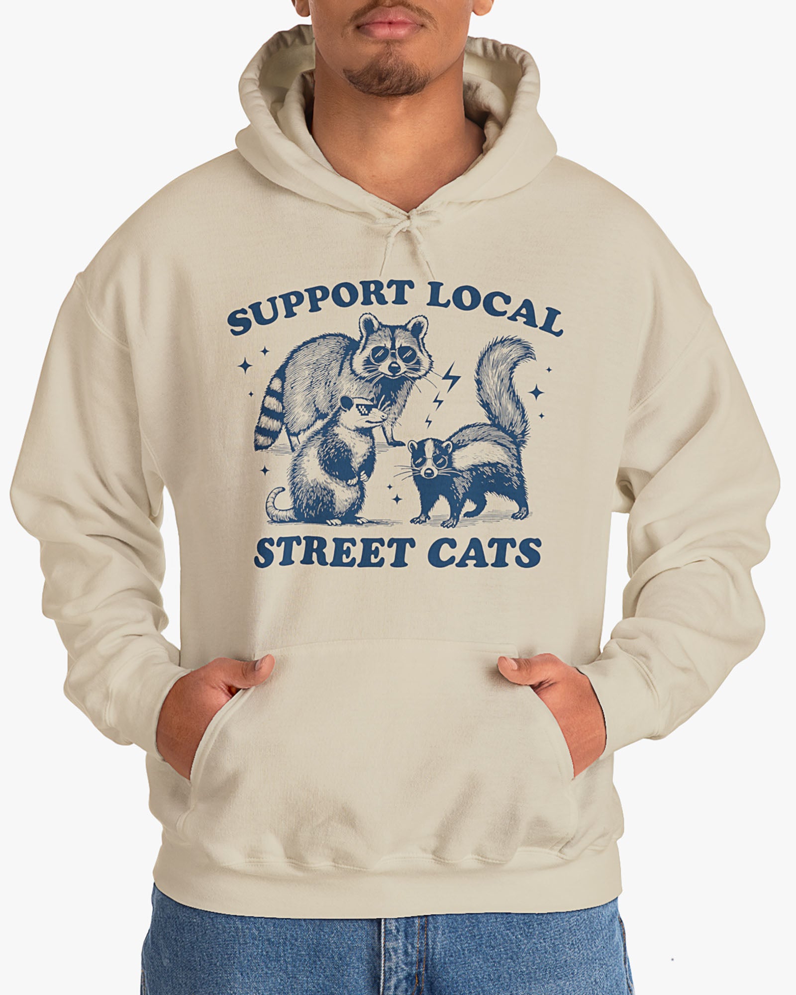 Man wearing sand beige 'Support Local Street Cats' hoodie with a funny raccoon and opossum retro graphic