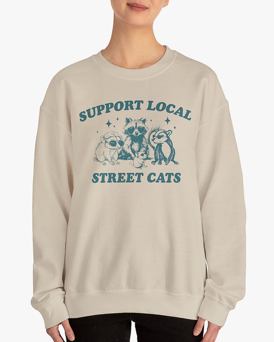 Woman wearing sand beige 'Support Local Street Cats' sweatshirt with funny retro raccoon and opossum graphic