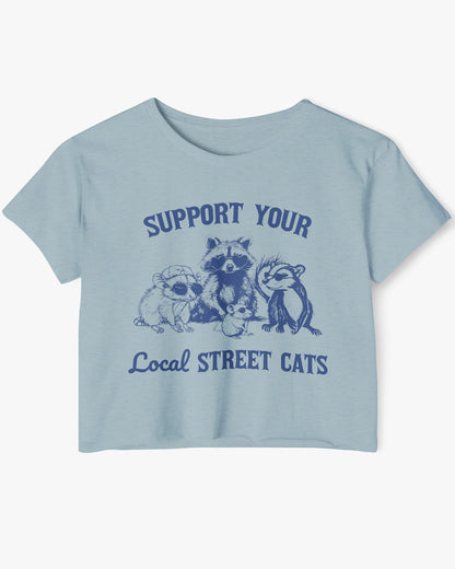 Flat lay of a stonewash denim 'Support Your Local Street Cats' crop top featuring a funny retro raccoon ang graphic.