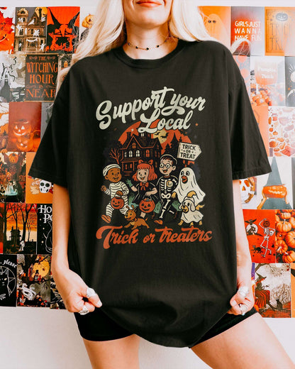 Woman wearing a black ‘Support Your Local Trick Or Treaters’ shirt with a retro Halloween graphic of kids trick-or-treating near a haunted house.