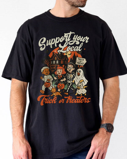 Man wearing a black ‘Support Your Local Trick Or Treaters’ shirt with a retro Halloween graphic of kids trick-or-treating near a haunted house.