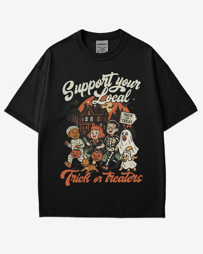 Flat lay black ‘Support Your Local Trick Or Treaters’ shirt with retro Halloween graphic of kids trick-or-treating near a haunted house.