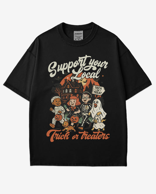 Flat lay black ‘Support Your Local Trick Or Treaters’ shirt with retro Halloween graphic of kids trick-or-treating near a haunted house.