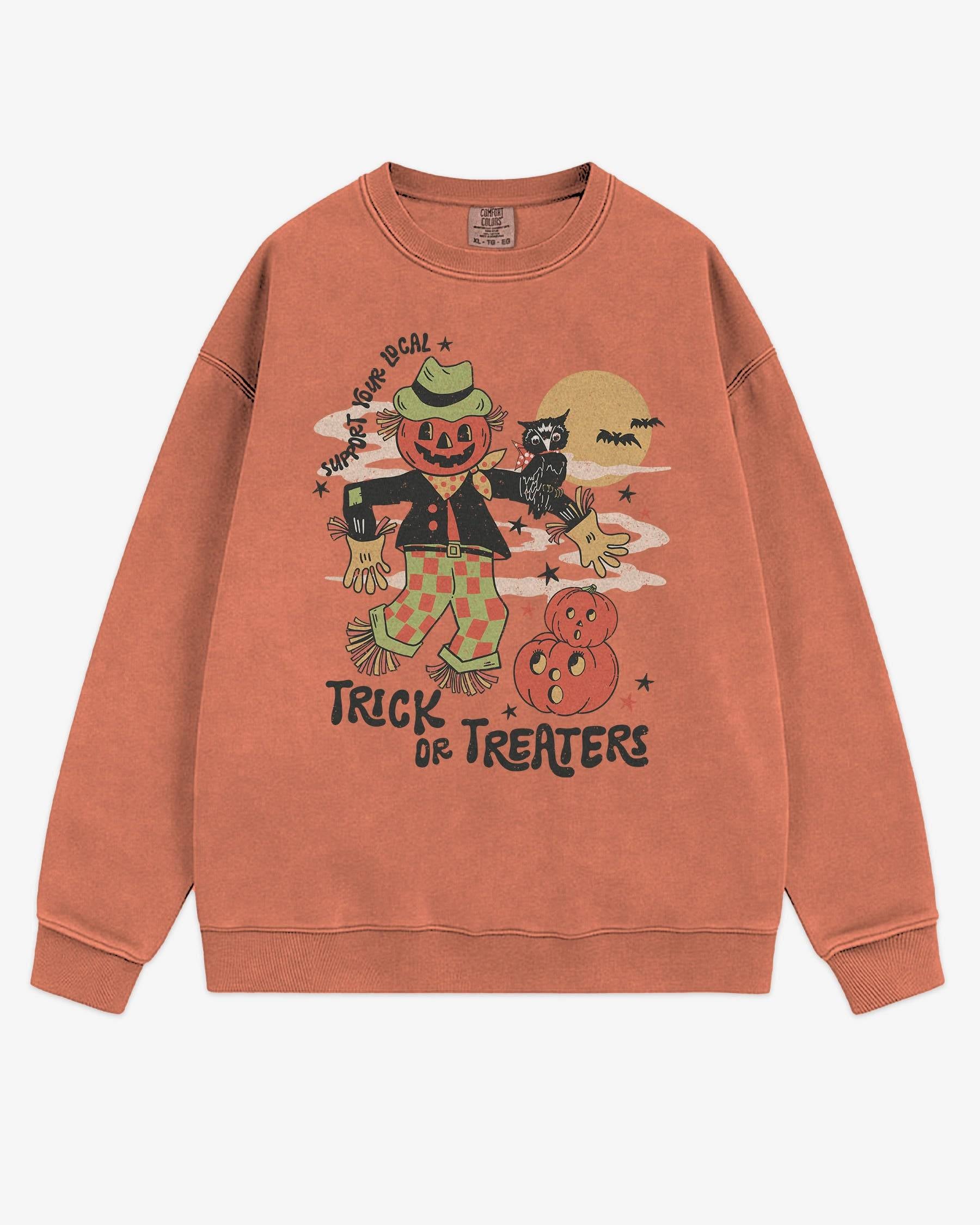 Flat lay terracotta Halloween sweatshirt reading ‘Support Your Local Trick Or Treaters’ with retro graphic of scarecrow, owl, and pumpkins.