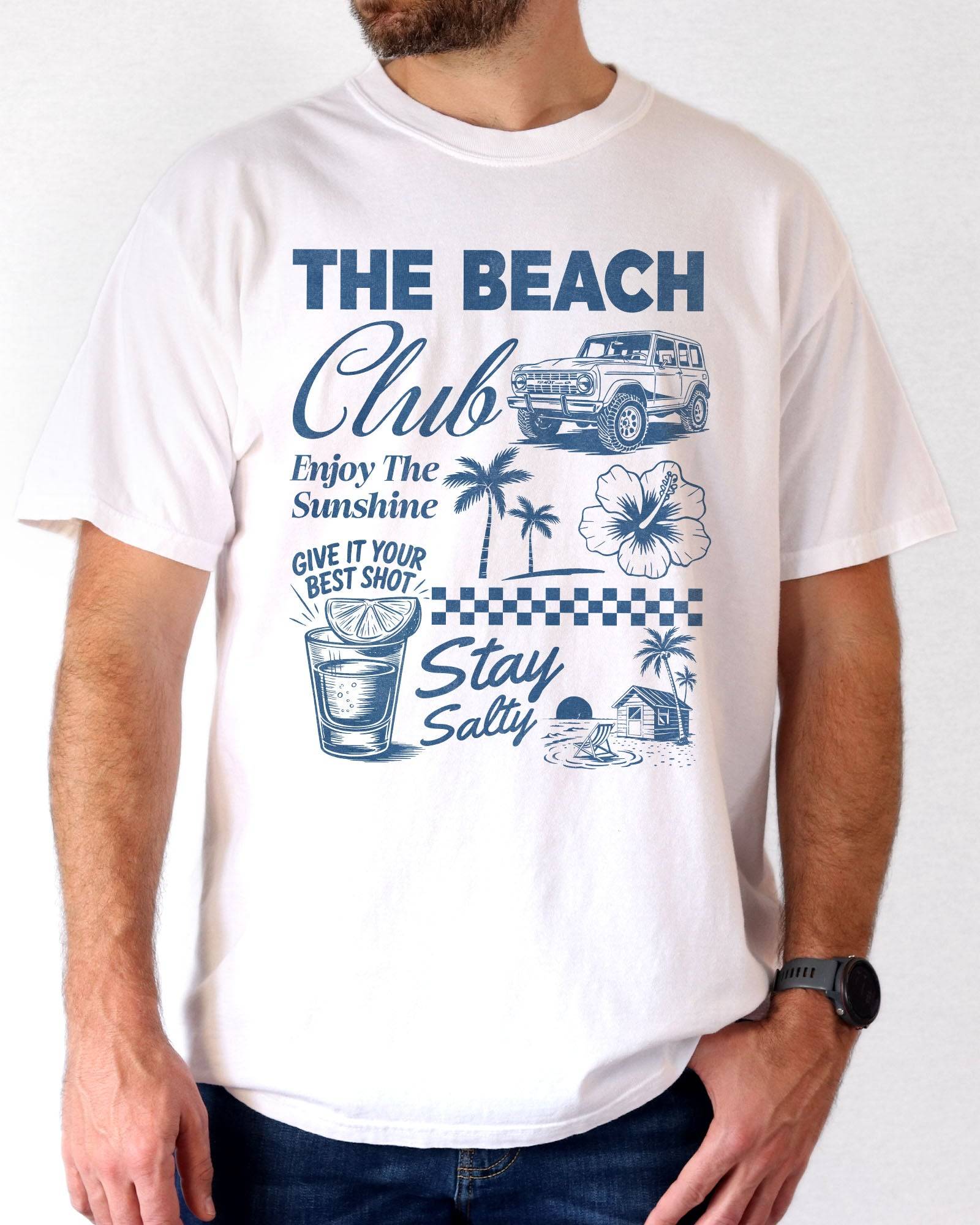 Man wearing a white “The Beach Club” shirt with a retro summer collage of sunshine, beach, and drinks.