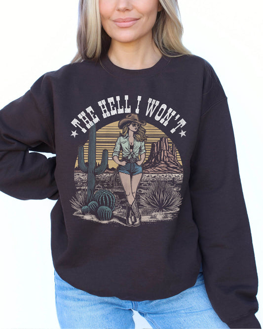 Woman wearing a dark chocolate-colored sweatshirt with an 80s retro graphic of a cowgirl in a western desert scene and the quote "The Hell I Won’t".