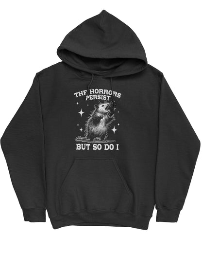 Flat lay of a black 'The Horrors Persist But So Do I' hoodie featuring a funny retro yelling opossum graphic.