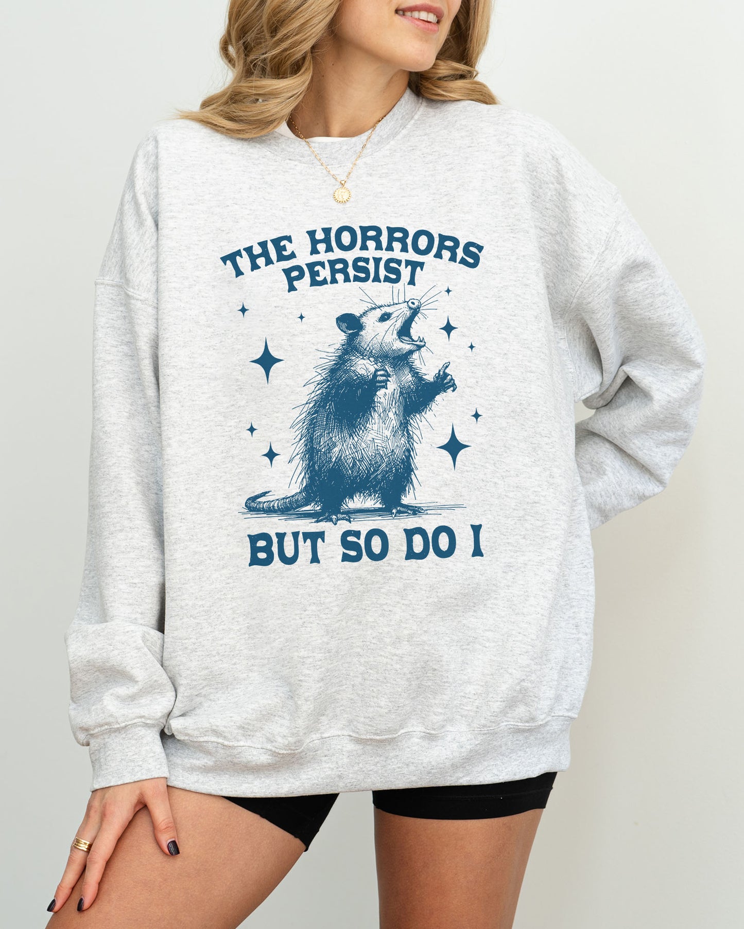 Model wearing ash color sweatshirt with 'The Horrors Persist, But So Do I' graphic design