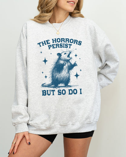 Model wearing ash color sweatshirt with 'The Horrors Persist, But So Do I' graphic design