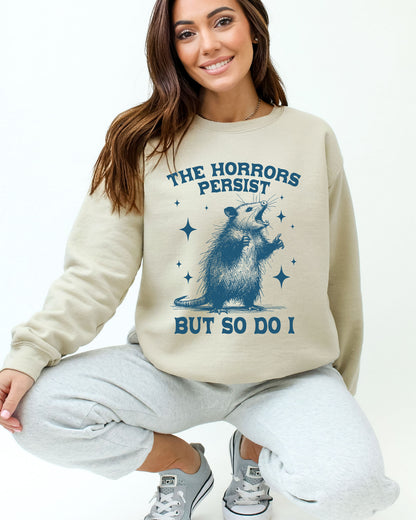 Model wearing sand color sweatshirt with 'The Horrors Persist, But So Do I' graphic design