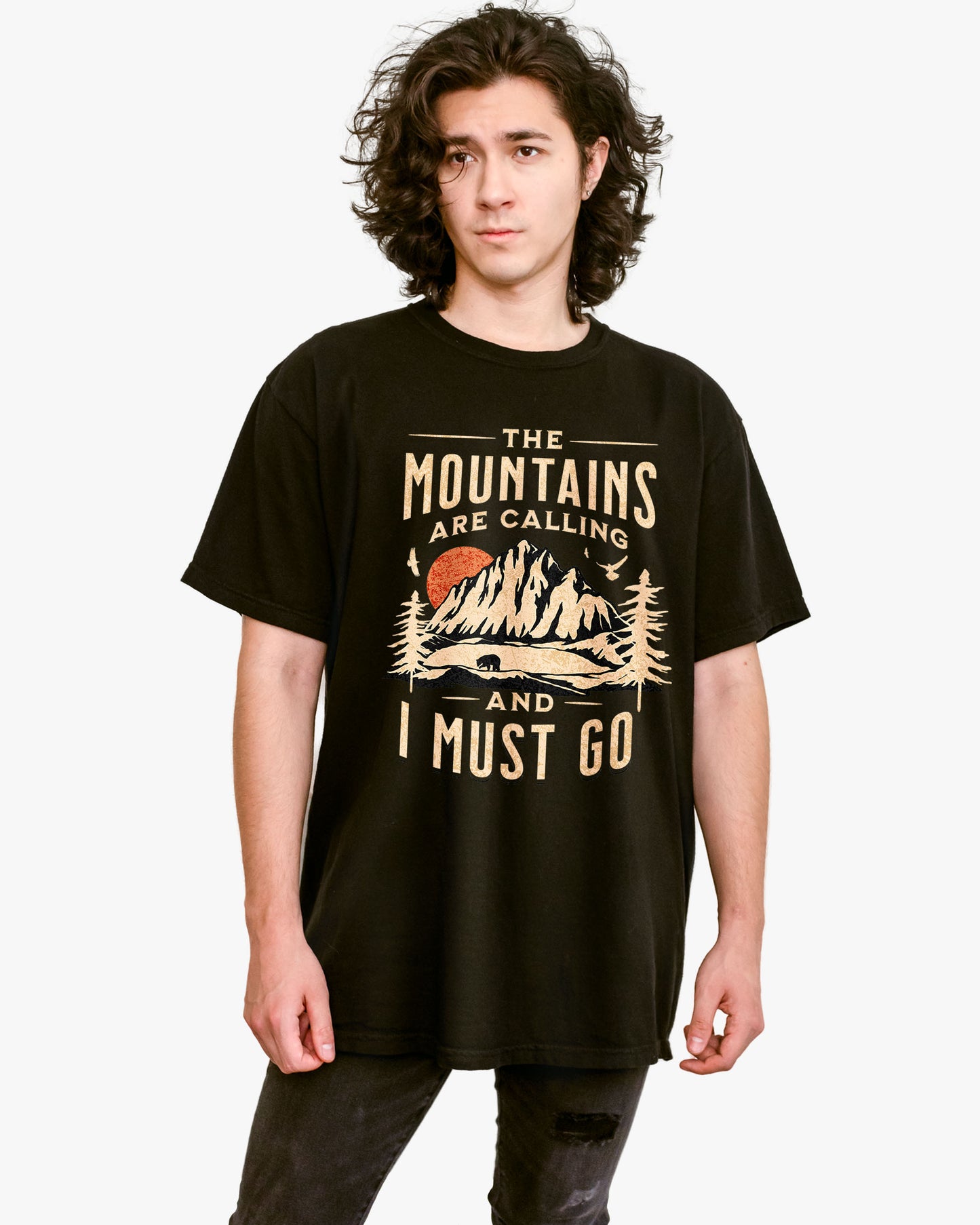 Man wearing black shirt with phrase ‘The Mountains Are Calling And I Must Go’ and retro mountain nature graphic.