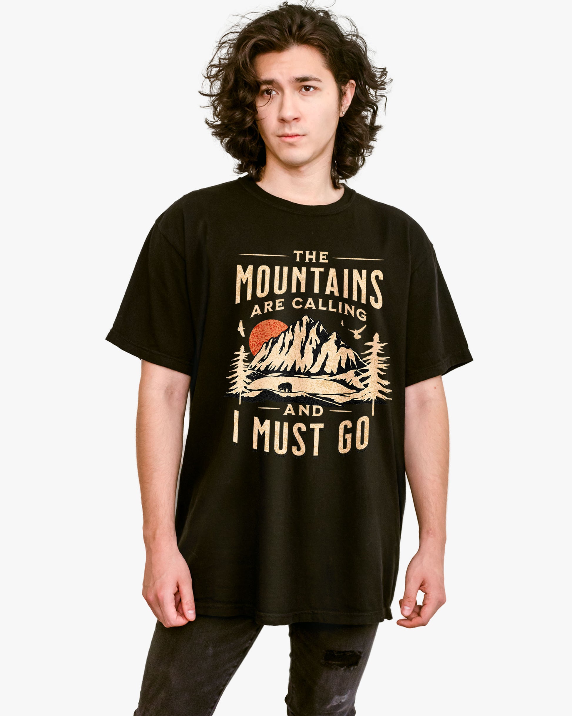 Man wearing black shirt with phrase ‘The Mountains Are Calling And I Must Go’ and retro mountain nature graphic.