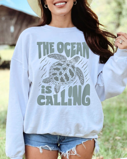 Model wearing white color sweatshirt with 'The Ocean Is Calling' graphic design