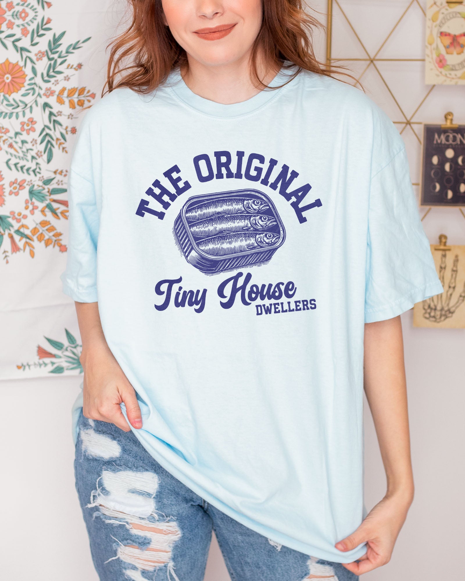 Woman wearing a chambray "The Original Tiny House Dwellers" shirt featuring a retro graphic of sardines packed in a tin can.