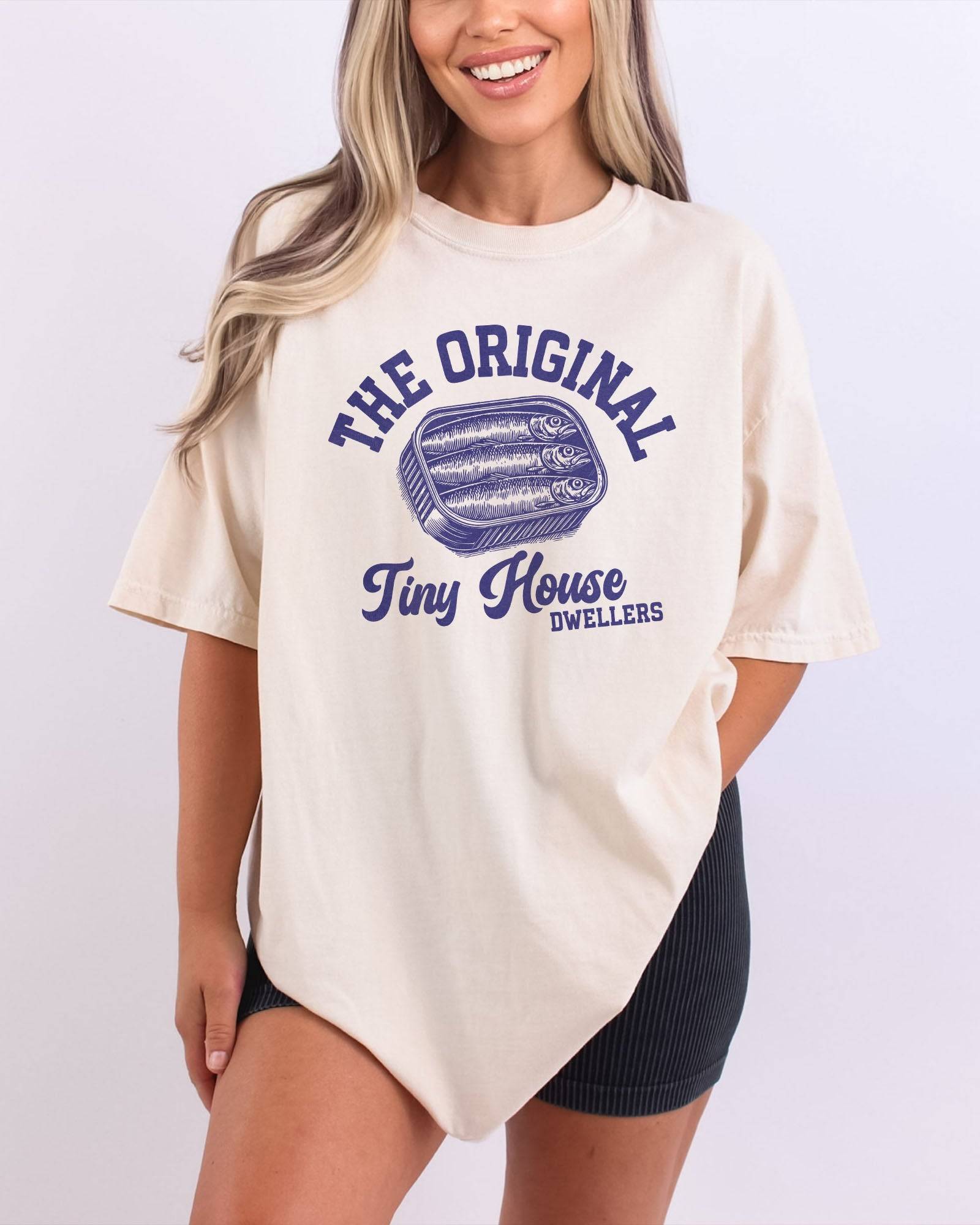 Woman wearing an ivory "The Original Tiny House Dwellers" shirt featuring a retro graphic of sardines packed in a tin can.