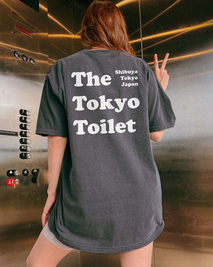 Woman wearing a pepper T-shirt with 'The Tokyo Toilet' text printed on the back, inspired by Shibuya's public toilets.