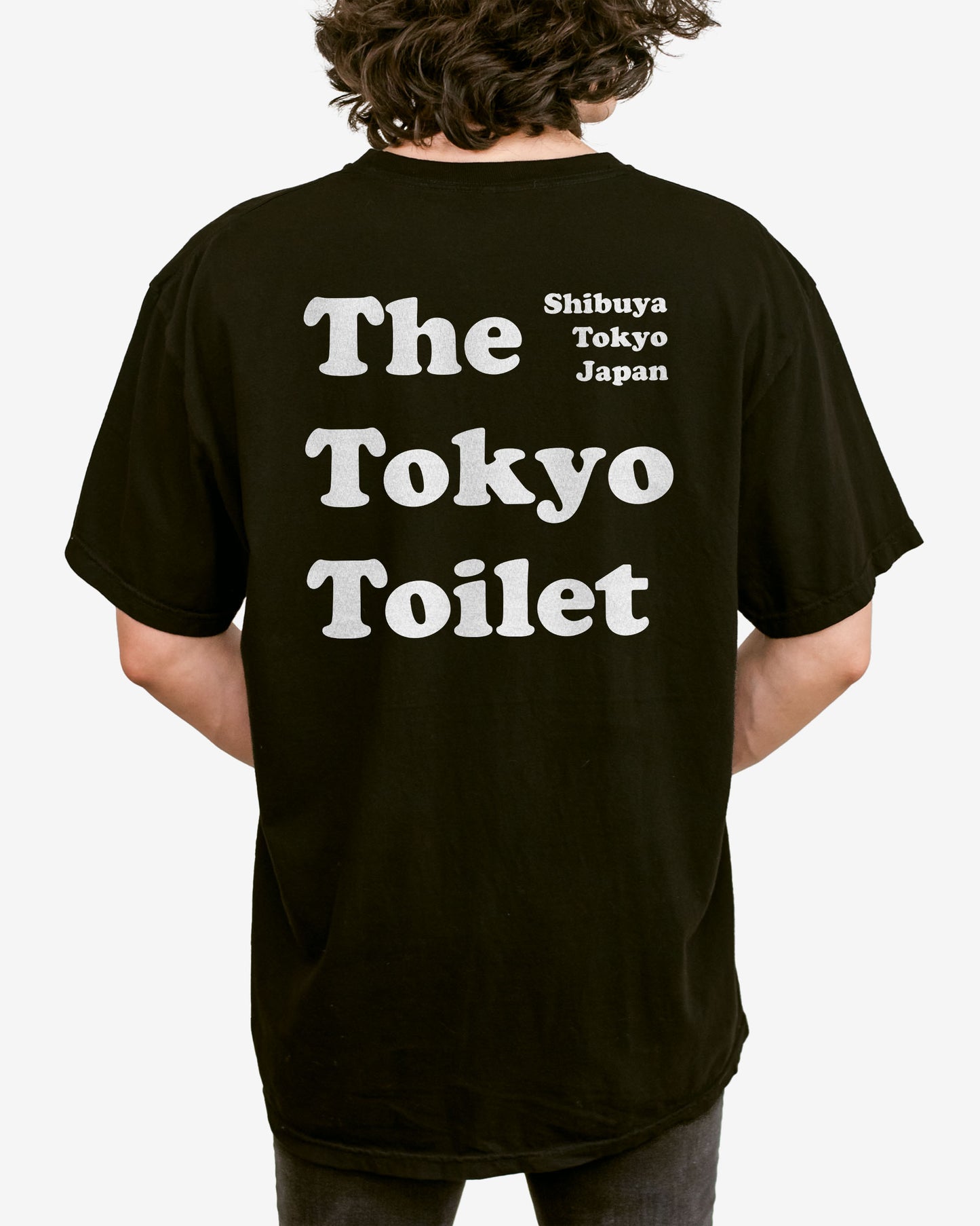 Man wearing a black T-shirt with 'The Tokyo Toilet' text printed on the back, inspired by Shibuya's public toilets.