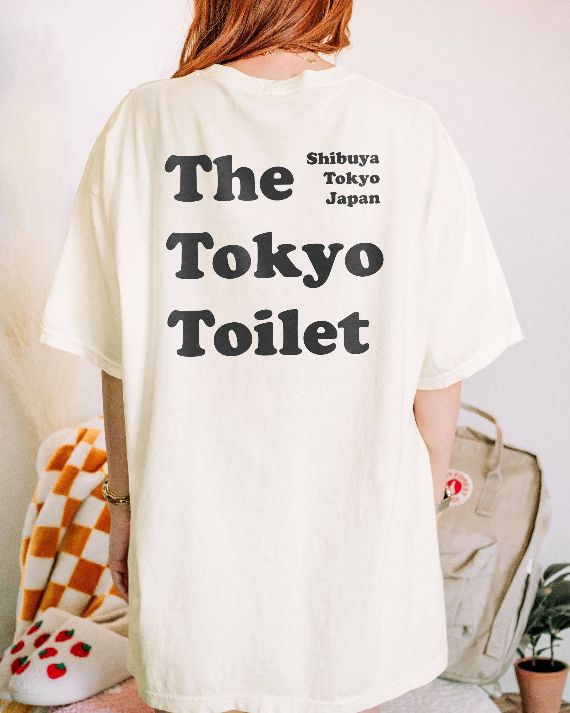 Woman wearing an ivory T-shirt with 'The Tokyo Toilet' text printed on the back, inspired by Shibuya's public toilets.