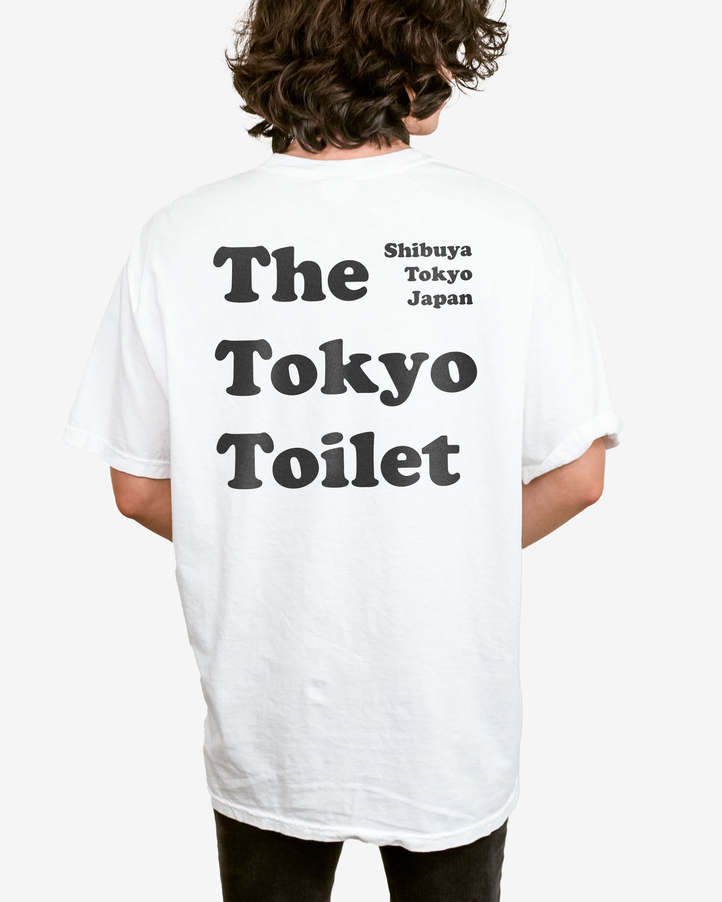 Man wearing a white T-shirt with 'The Tokyo Toilet' text printed on the back, inspired by Shibuya's public toilets.