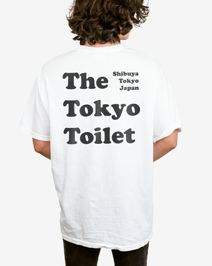 Man wearing a white T-shirt with 'The Tokyo Toilet' text printed on the back, inspired by Shibuya's public toilets.