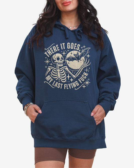 Woman wearing true navy 'There It Goes My Last Flying Fuck' hoodie with funny retro skeleton and bat Halloween graphic.