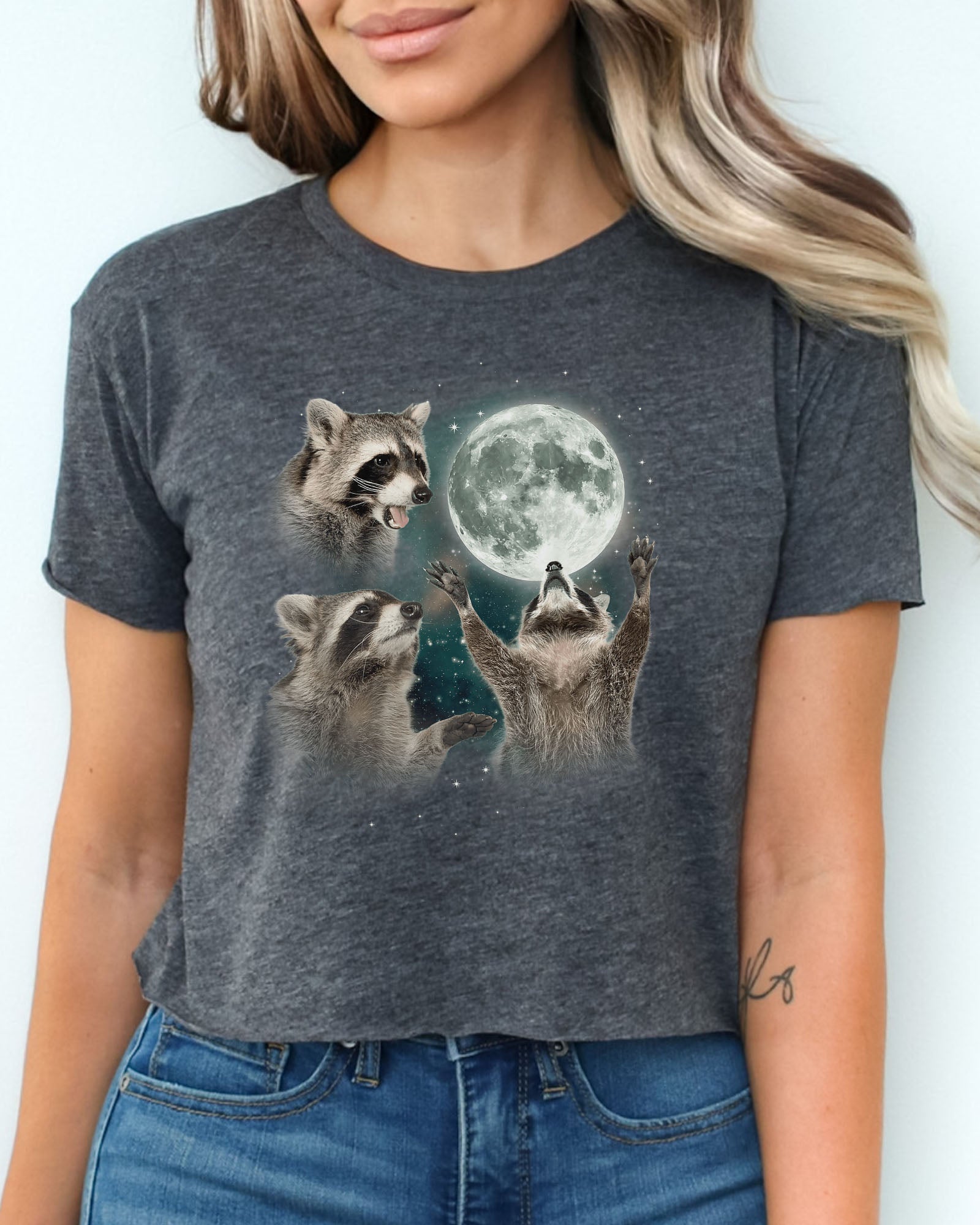 Charcoal gray crop top with a retro graphic of three raccoons howling at the moon, worn by a woman.