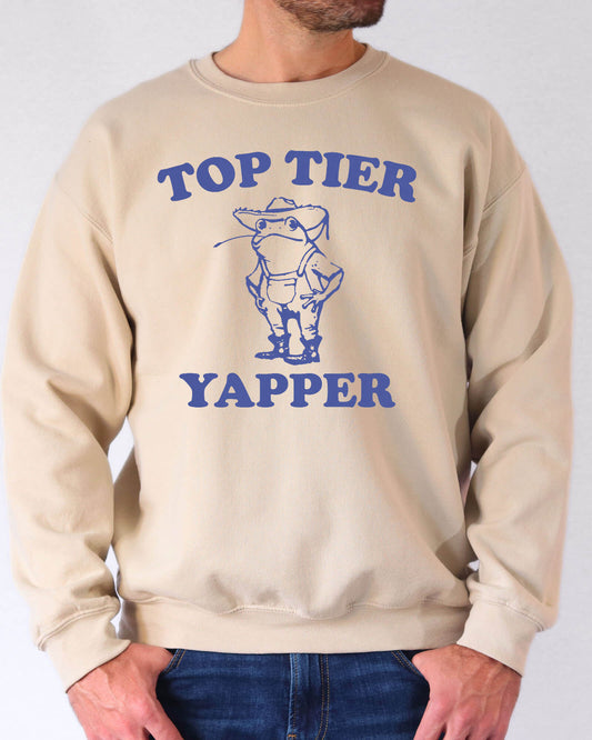 Man wearing a sand beige sweatshirt featuring a funny retro country frog graphic and the quote 'Top Tier Yapper'.