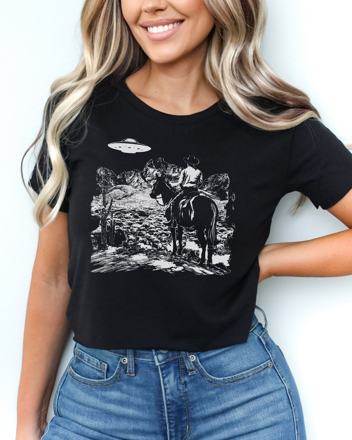 Woman wearing black crop top featuring a UFO and western desert scenery graphic.