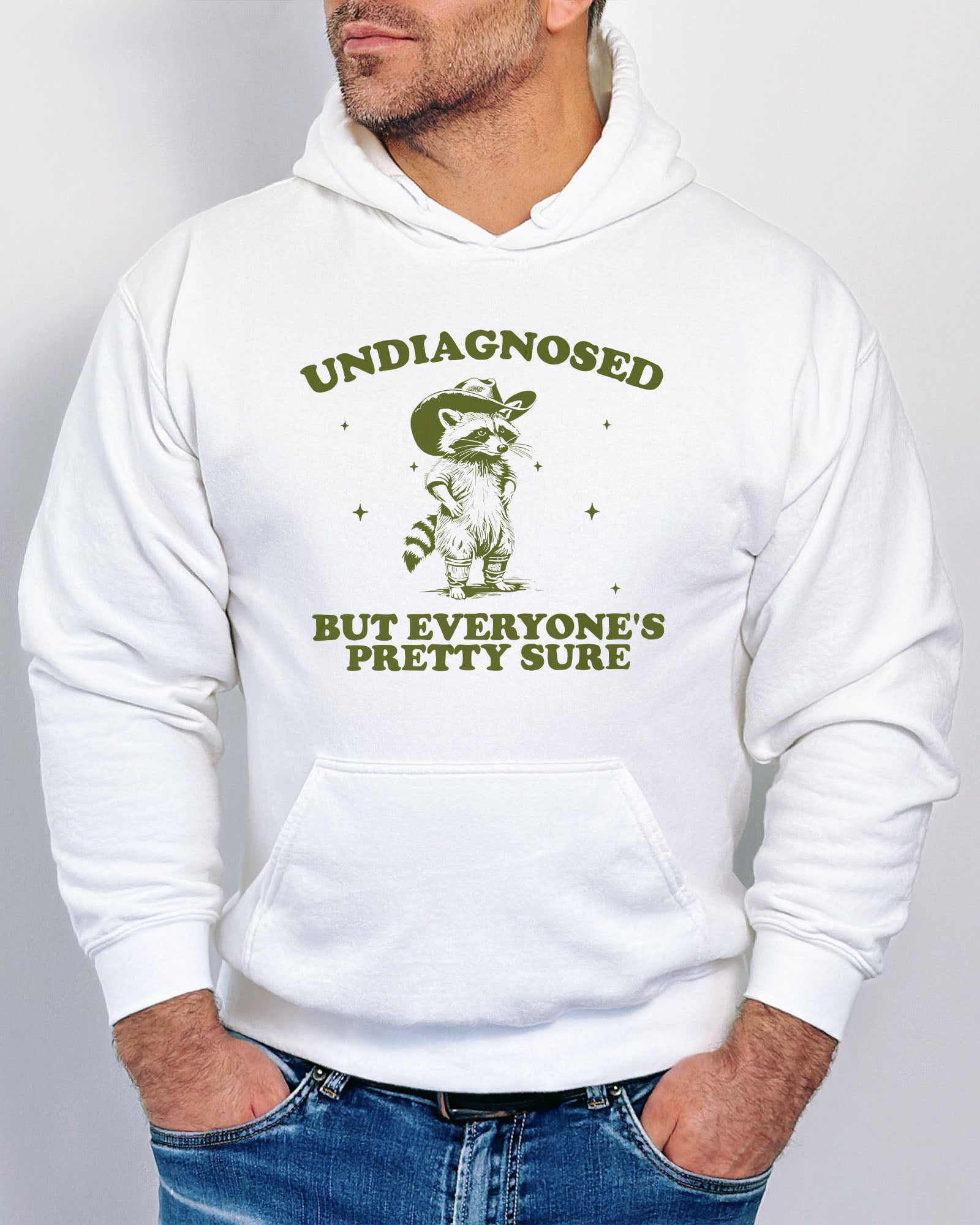 Man wearing white hoodie with a funny retro cowboy raccoon graphic and the quote 'Undiagnosed, But Everyone's Pretty Sure'.