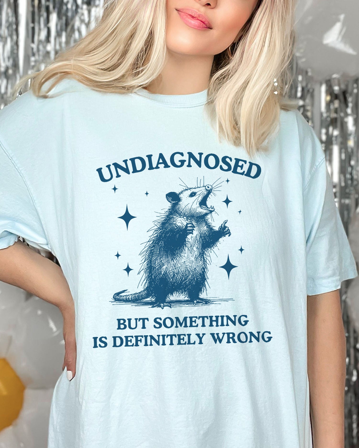 Woman wearing an oversized light blue 'Undiagnosed, But Something Is Definitely Wrong' t-shirt featuring a funny opossum graphic.